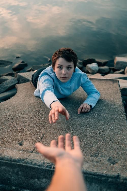 Woman reaching out for help, on a stone with water in the back